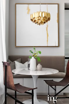 a white table with two brown chairs and a painting on the wall above it in a living room