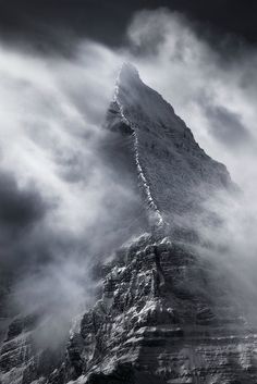 a very tall mountain in the middle of some foggy skies with clouds around it