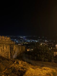 the city lights shine brightly in the dark night sky over an old wall and fence