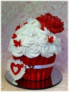 a cupcake decorated with white frosting and red flowers on a glass platter