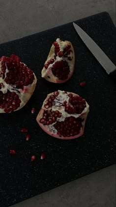 three pomegranates on a cutting board with a knife