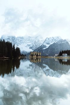 a large body of water surrounded by snow covered mountains and pine trees in the foreground