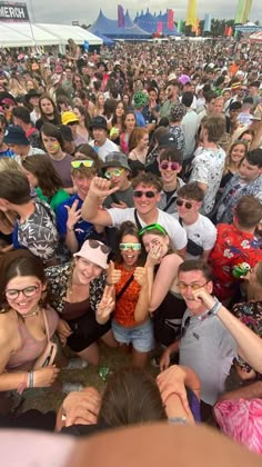 a large group of people standing around each other at a music festival with their hands up in the air