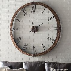 a large wooden clock mounted to the side of a white brick wall above a gray couch