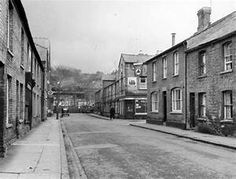 an old black and white photo of a street with brick buildings on both sides, in the middle of town