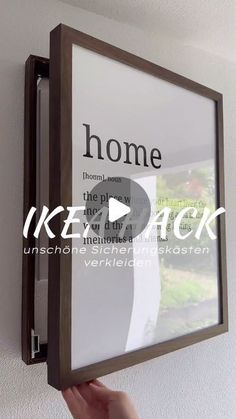 a person is holding up a frame with the words home on it in front of a white wall