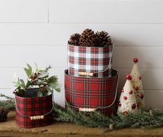 three plaid christmas boxes with pine cones on top and evergreen branches in the bottom, sitting next to each other