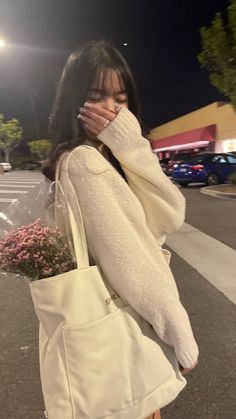 a woman is walking down the street with her hand on her face while holding a flower