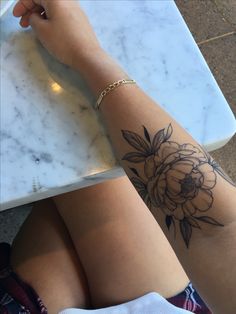 a woman sitting at a table with a flower tattoo on her arm and leg,