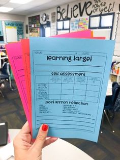 a person holding up three blue and pink learning target posters in front of a classroom