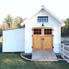 a small white barn with two doors and a wooden walkway leading up to the front door