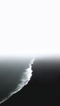 an airplane flying over the ocean on a foggy day with black and white waves