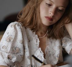 a woman sitting at a table writing on a piece of paper with a pen in her hand