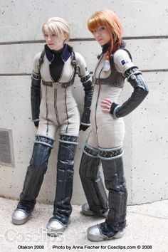 two women dressed in futuristic garb standing next to each other on the side of a building