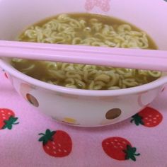 a bowl filled with noodles and chopsticks on top of a pink table cloth