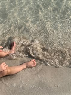 two people are sitting on the beach with their feet in the water