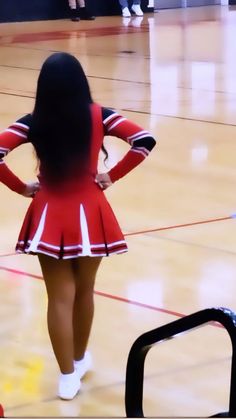 a girl in a cheerleader uniform is standing on the court with her hands behind her back