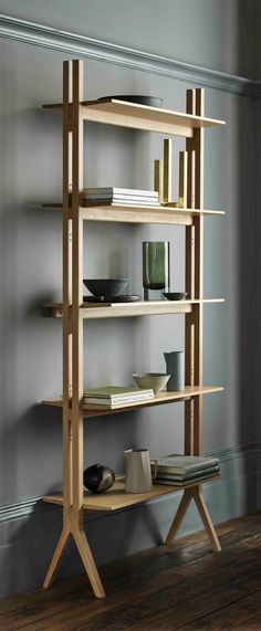 a wooden shelf with many books on top of it in front of a gray wall