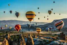 many hot air balloons are flying in the sky over rocks and mountains at sunrise or sunset