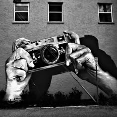 a black and white photo of a person holding a camera in front of a building