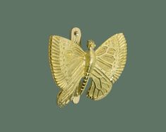 a gold brooch with a large butterfly on it's back, sitting against a green background