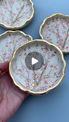 hand holding three decorative dishes with pink and white designs on them in front of a blue background