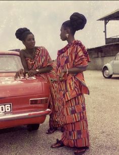 two women standing next to an old red car