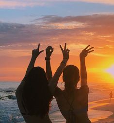 two women standing on the beach with their arms in the air