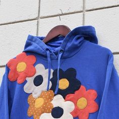 a blue hoodie with flowers on it is hanging against a brick wall in front of a hanger