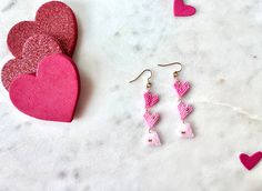 two pink heart shaped earrings sitting next to each other on a white table with hearts