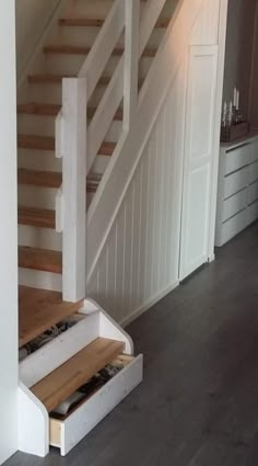 an open drawer underneath a stair case in a room with white walls and wood floors