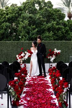 a man and woman standing in front of an aisle with flowers on the ground next to them