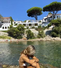 a woman sitting on top of a rock next to the ocean with houses in the background