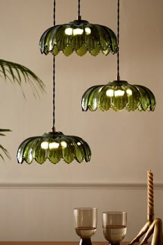 three green glass lights hanging from the ceiling above a wooden table with two wine glasses on it