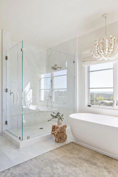 a white bathroom with a tub, chandelier and large glass shower stall in the corner