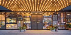 an entrance to a restaurant with potted plants and lights on the front door at night