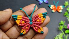 a hand holding a small beaded butterfly in front of some flowers and other beads