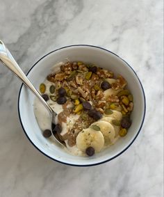 a bowl filled with granola and bananas on top of a marble counter next to a spoon