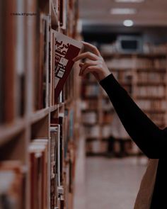 a woman is looking at books on the shelves in a library and she is reading