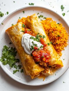 a white plate topped with two enchiladas next to rice and cilantro