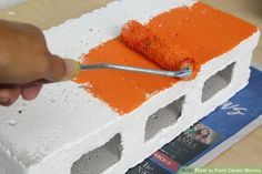 someone using a brush to paint a brick with orange and white colors on it,