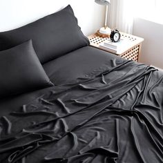 a bed with black sheets and pillows on top of it next to a window in a bedroom