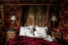 a bed with red sheets and white pillows in a room that has wall paper on the walls