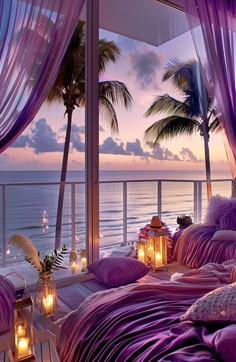 a bed with purple sheets and pillows next to the ocean