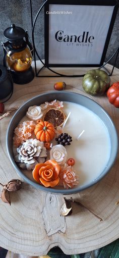 a candle is sitting in a bowl with flowers and leaves on the table next to it