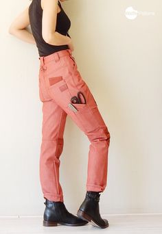 a woman in black shirt and pink pants standing next to wall with scissors on it