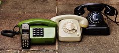 three old - fashioned telephones are sitting on the ground, one green and one black