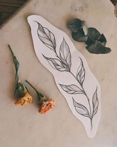 two dried flowers on a table next to a piece of paper with leaves drawn on it