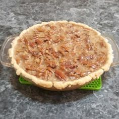 a pecan pie sitting on top of a green plastic container with a glass lid