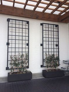 two black planters with plants in them on the side of a white brick building